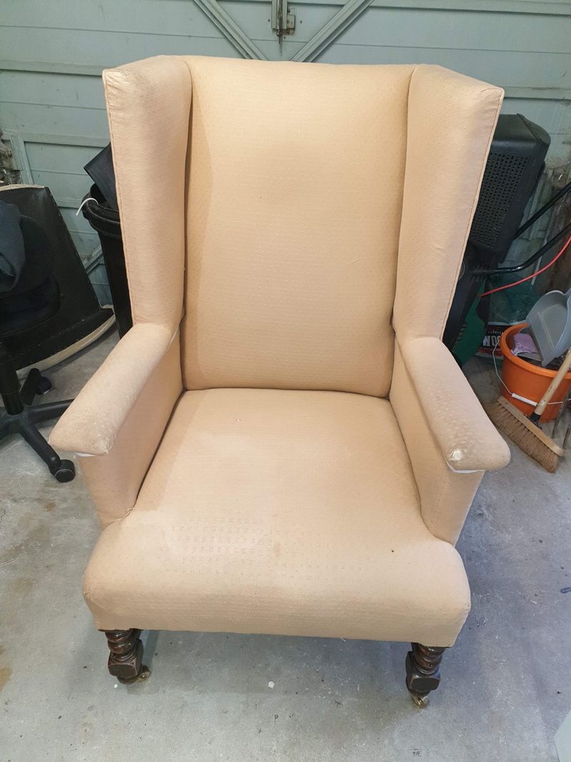 Wing chair before its new slipcover, in worn peach upholstery